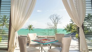 Habitación con vistas al océano, que incluye una mesa con sillas, ventanas amplias con cortinas y suelo de madera.