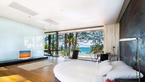 A modern bedroom with a large bed, a TV, and a view of the ocean.