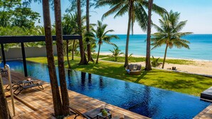 A pool area with wooden decking, lounge chairs, and a view of the beach and ocean.
