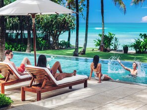A poolside area with lounge chairs and a large umbrella, surrounded by palm trees and a view of the ocean. - Villa Nandana 7BR, Beachfront, Gym, Maid, BF (Takua Thung)