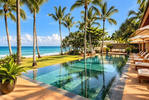 A pool with a view of the ocean, surrounded by palm trees and lounge chairs.