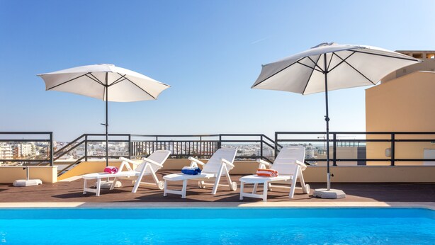 A rooftop pool with white lounge chairs and umbrellas, overlooking a cityscape. - 2-Bedroom Apartment with Rooftop Pool, Village Marina, Olhão (Olhão)