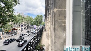 A busy street with cars and a bus, a balcony with a railing, and a building facade. - Urban Flat 60 - Sublime Parisian Flat in Paris (París)
