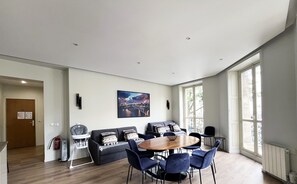 A modern living room with a dining area, a sofa set, and a large window providing natural light.