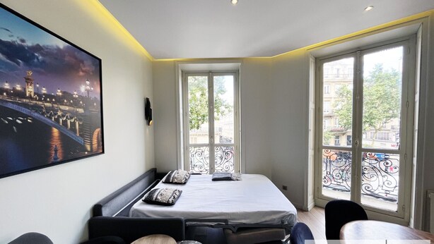 A bedroom with a bed, a desk, and a large window with a view of a bridge and buildings. - Urban Flat 60 - Sublime Parisian Flat in Paris (París)