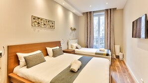 Ein Hotelzimmer mit zwei Betten, einem Flachbildfernseher, einem Fenster mit Vorhängen und einem dekorativen Wandbild.