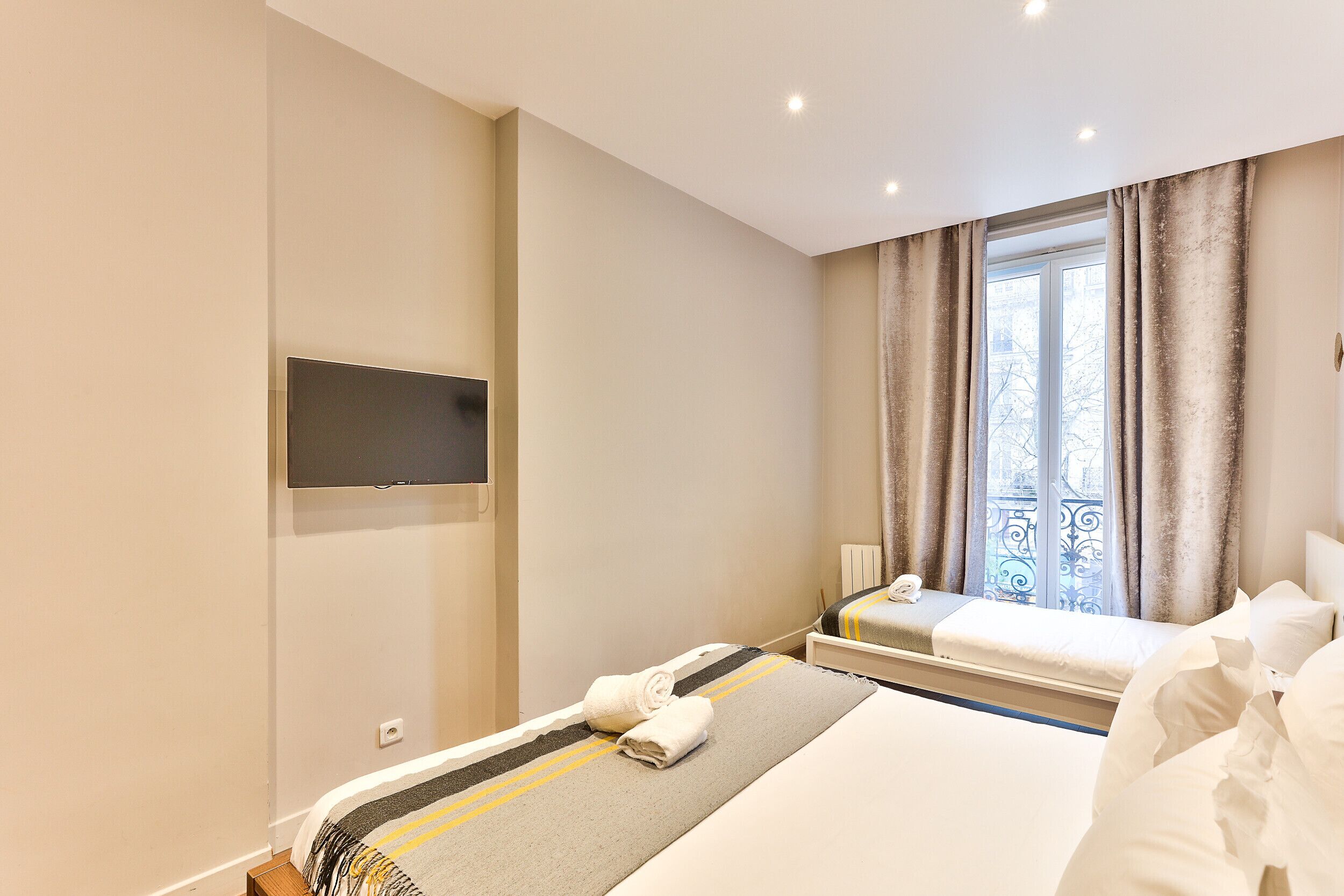 A hotel room with a bed, a TV mounted on the wall, a window with curtains, and a view of the outside.