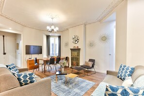 Un salon comprenant un canapé, un fauteuil, une table basse et un téléviseur. Il y a également un coin repas avec des chaises et une table.