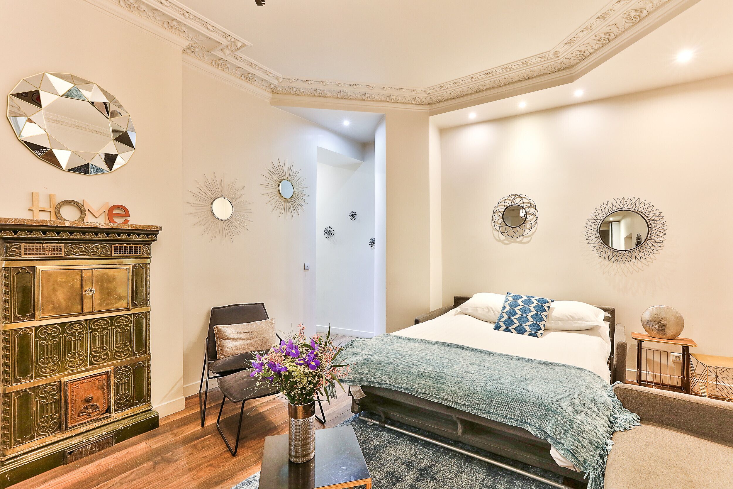 A bedroom with a bed, a dresser, a chair, and decorative mirrors.