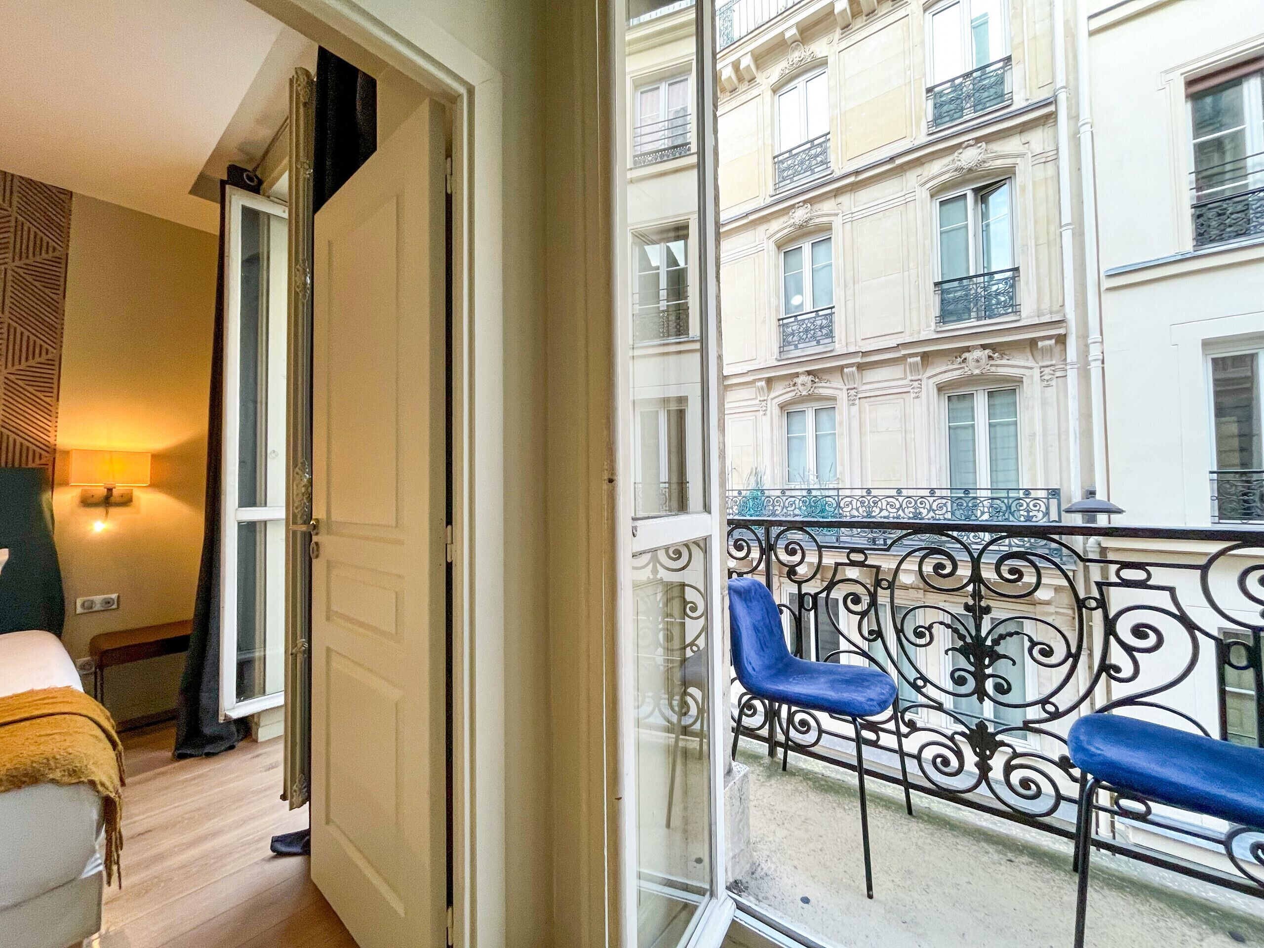 Une chambre avec un balcon, un lit, une chaise et une lampe.