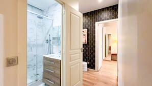 Un bagno moderno con box doccia in vetro, mobile lavabo in legno e pannello di marmo.