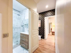 Un baño moderno con cabina de ducha de vidrio, tocador de madera y salpicadero de mármol.