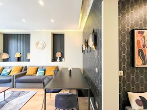 Una sala de estar moderna con un sofá, una mesa de comedor y sillas. Hay adornos en la pared y un cuadro.