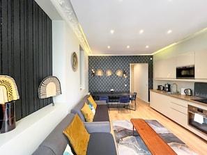 A modern living room with a sofa, a dining table, and a kitchen area with appliances.