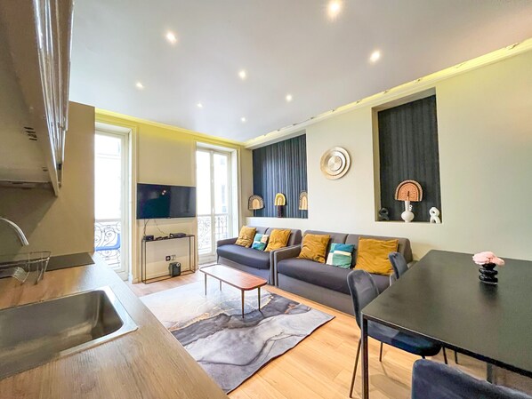 Uma sala de estar moderna com um sofá, mesa de centro e mesa de jantar. Há uma área de cozinha com pia e televisão.