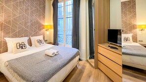 Una camera d'albergo con un letto, una televisione, un comò in legno e una finestra con tende.