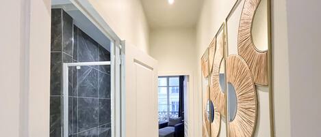 Un couloir avec une porte en verre donnant sur un balcon, un mur orné de miroirs décoratifs et un coin salon offrant une vue sur l’extérieur.