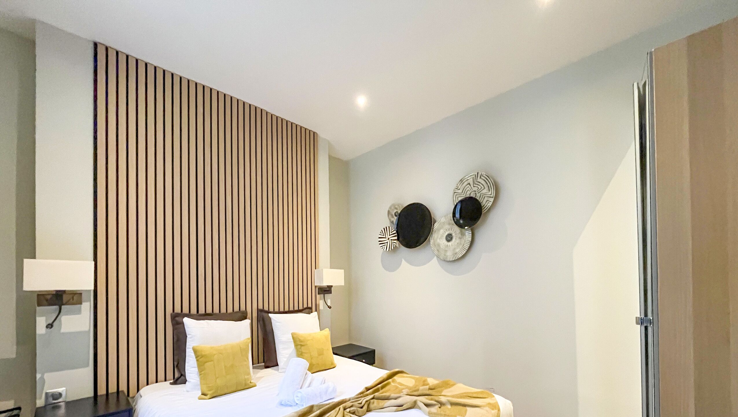Een moderne hotelkamer met een bed, nachtkastjes, een wandlamp en decoratieve muurkunst.