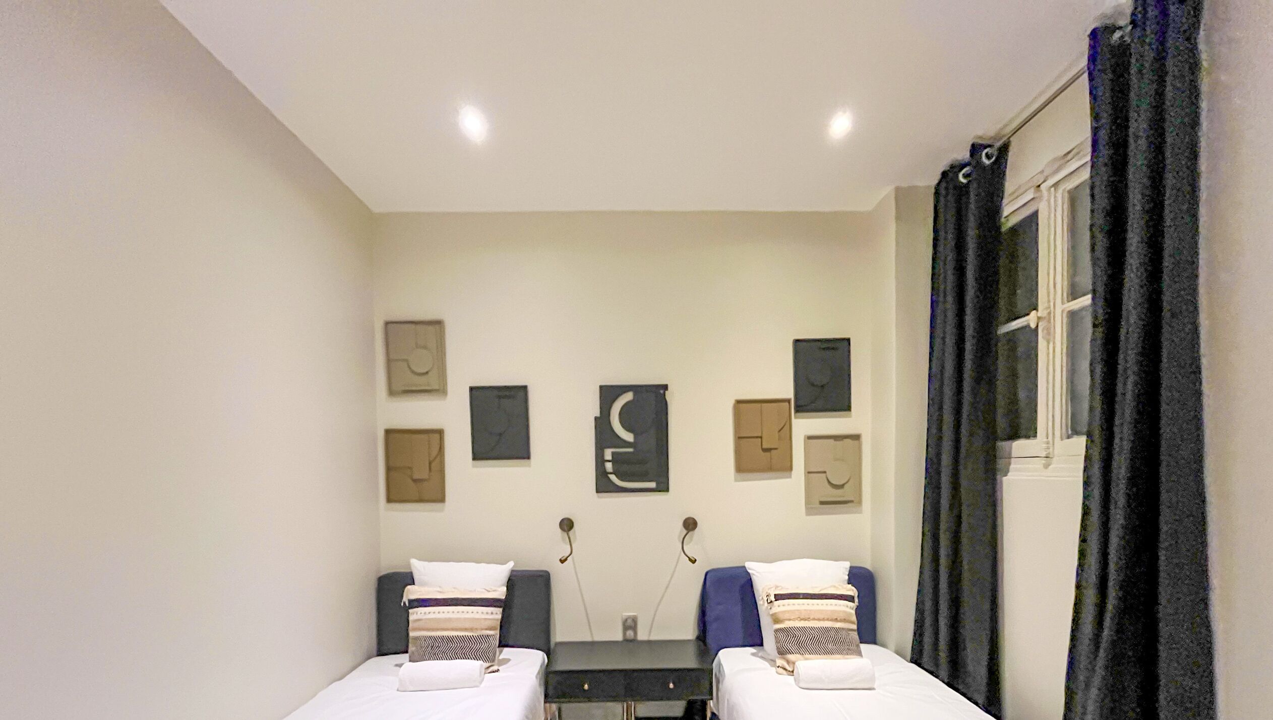 Une chambre d’hôtel avec deux lits simples, une petite table et des œuvres d’art abstraites accrochées au mur.