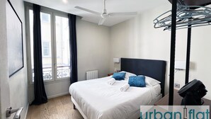 Una moderna camera d'hotel con un letto grande, una ventola a soffitto, una finestra con tende e vista sulla città.