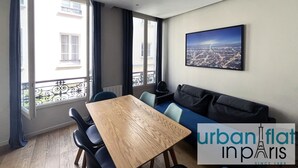Un soggiorno moderno con un tavolo in legno, sedie blu, un divano scuro e vista sulla città.