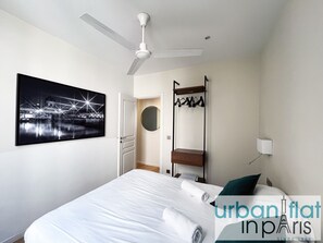 A hotel room with a bed, a ceiling fan, a wall-mounted TV, a coat rack, and a mirror.