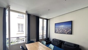 Una sala moderna con una mesa de madera, sillas azules, un sofá oscuro y vistas a un paisaje urbano.