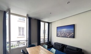 Un salon moderne avec une table en bois, des chaises bleues, un canapé foncé et une vue sur la ville.