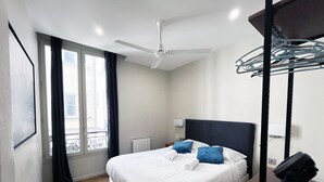 Una habitación de hotel moderna con una cama grande, un ventilador de techo, una ventana con cortinas y vistas a la ciudad.