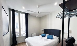 Une chambre d’hôtel moderne avec un grand lit, un ventilateur de plafond, une fenêtre avec des rideaux et une vue sur la ville.