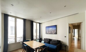 Un salon moderne avec une table à manger en bois, un canapé bleu et un tableau représentant un paysage urbain accroché au mur.