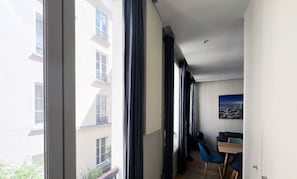 Un appartement moderne doté de grandes fenêtres, d’un balcon et d’un coin repas avec des chaises bleues.