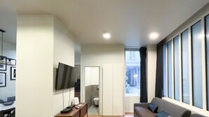 A modern living room with a flat-screen TV, a sofa, and a large window with curtains.