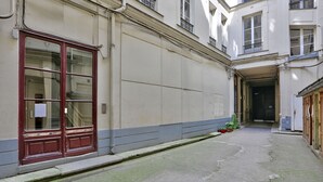 A narrow alleyway with a red door and a small garden area with potted plants.