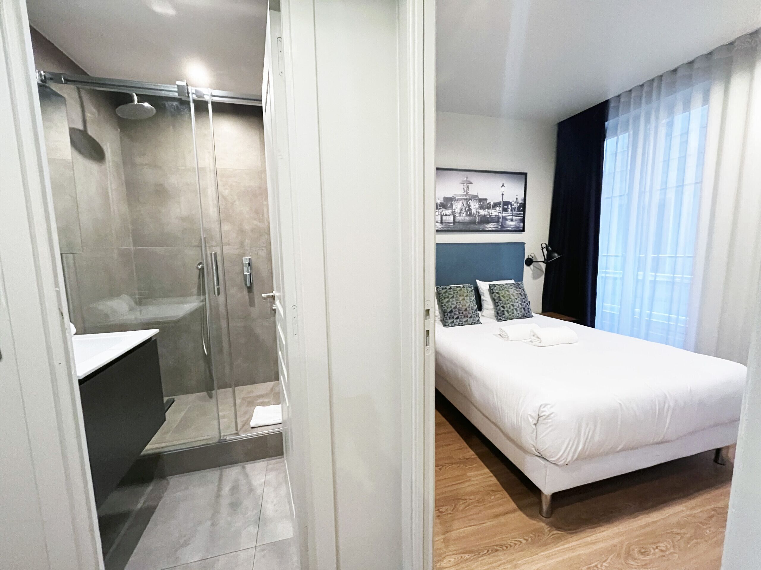 A modern hotel room with a shower, a bed, and a view of the city. - UrbanFlat 79 - Beautiful Large Apartment in Paris Le Marais (París)