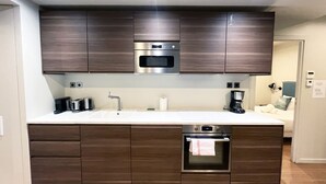 A modern kitchen with dark wooden cabinets, stainless steel appliances, and a white countertop. - UrbanFlat 79 - Beautiful Large Apartment in Paris Le Marais (París)