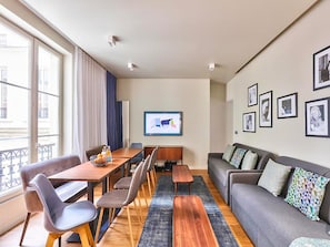 Una sala de estar moderna con un sofá, una mesa de comedor con sillas, una mesa de centro y un ventanal con cortinas.