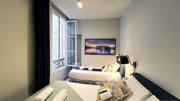 Habitación de hotel con dos camas, un ventanal con vistas, un cuadro en la pared y una lámpara de noche.
