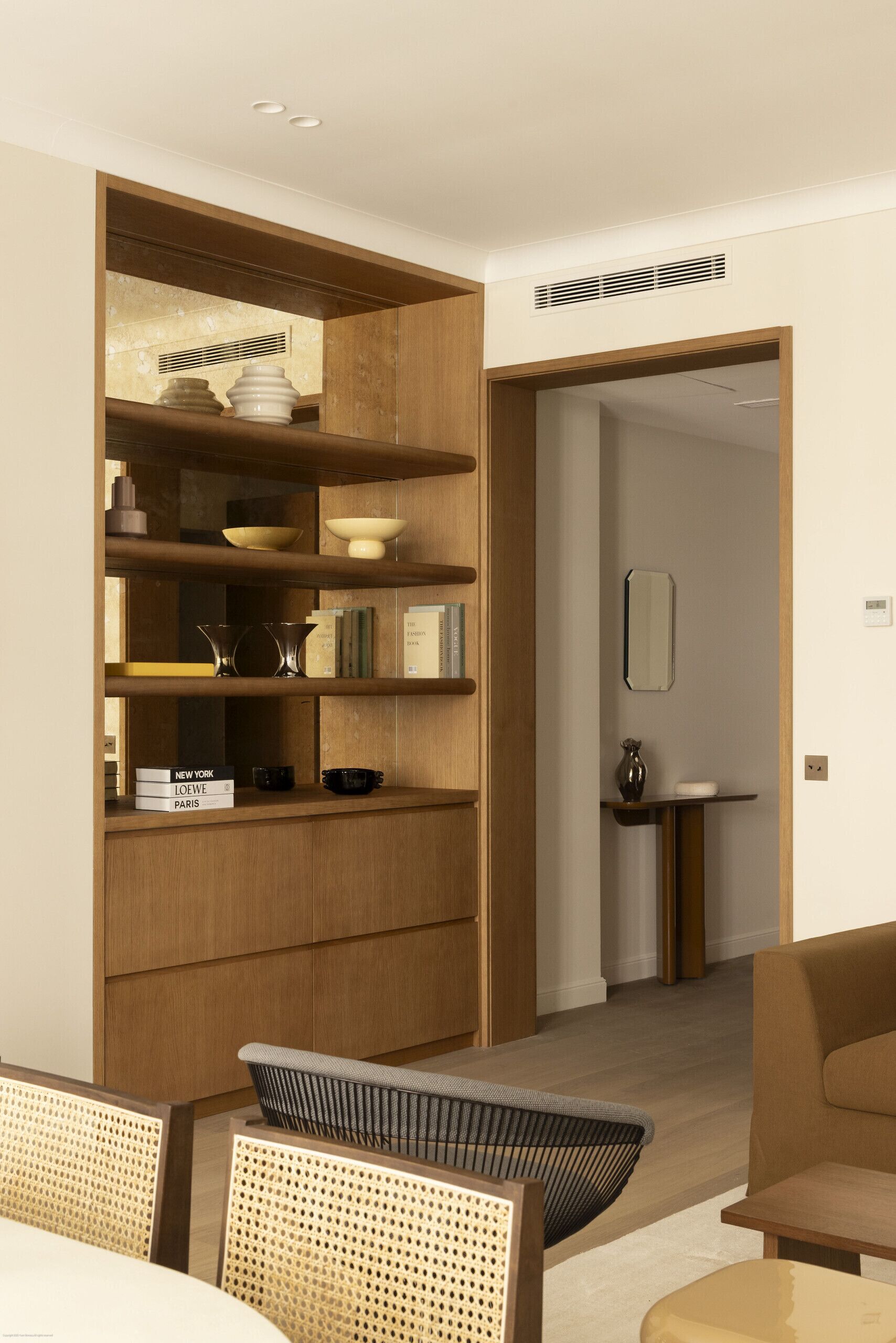 Ein modernes Interieur mit einer Holzeinrichtungsnische, einem Essbereich mit Korbstühlen und einem minimalistischen Badezimmer.