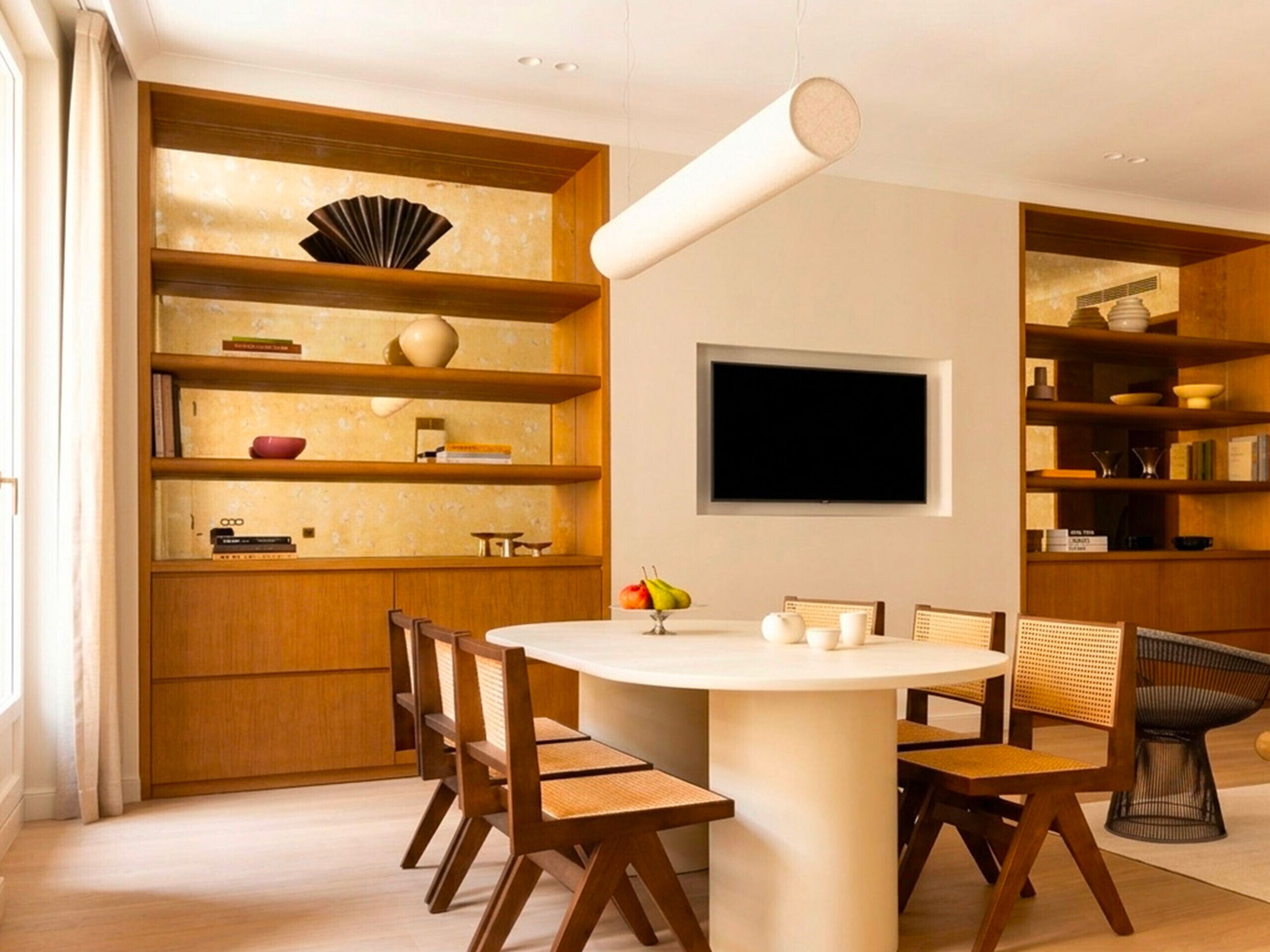 A modern dining area with a round table, wooden chairs, and built-in shelving with books and decorative items.