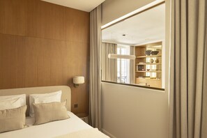A hotel room with a wooden headboard, a large mirror, a bedside table with a lamp, and a view of a balcony with bookshelves.