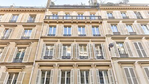 A multi-story building with symmetrical architecture, featuring evenly spaced windows with shutters, balconies with wrought iron railings, and decorative cornices.