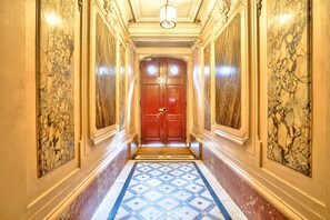A hallway with a marble floor, a red door with a brass handle, and a light fixture on the ceiling.