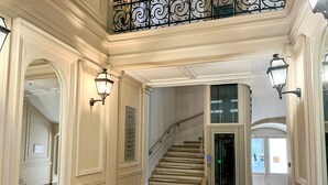 A grand hallway with a marble floor, a staircase, and ornate wall sconces. - 102 - Urban Opera Picasso (París)