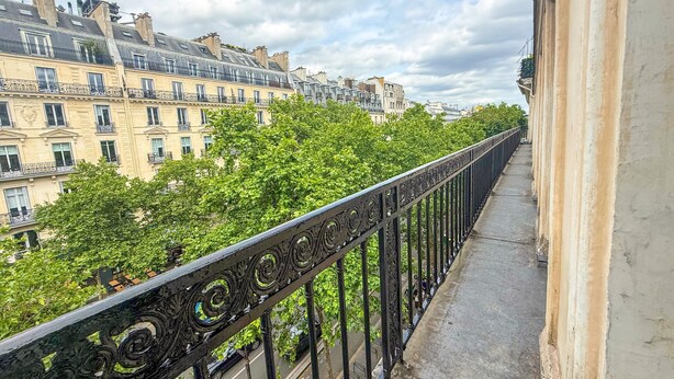 A balcony with ornate black railings overlooking a street lined with buildings and trees. - 102 - Urban Opera Picasso (París)