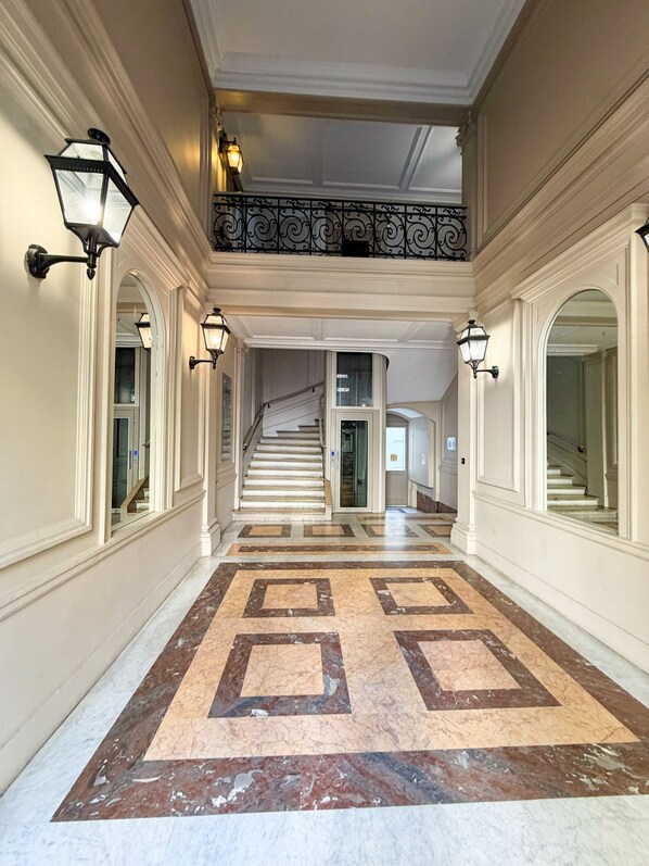 A grand hallway with a marble floor, a staircase, and wall sconces.
