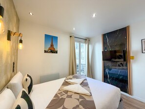 A hotel room with a bed, a painting of the Eiffel Tower, a large window with curtains, and a marble artwork on the wall.