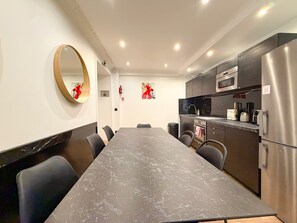 A modern kitchen with a marble countertop, stainless steel appliances, and a dining area with a long table and chairs.