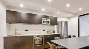 Una cocina moderna con armarios oscuros, horno empotrado, microondas y refrigerador de acero inoxidable.