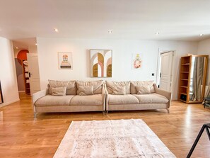 A living room with a beige sofa, a patterned rug, and a wooden floor.
